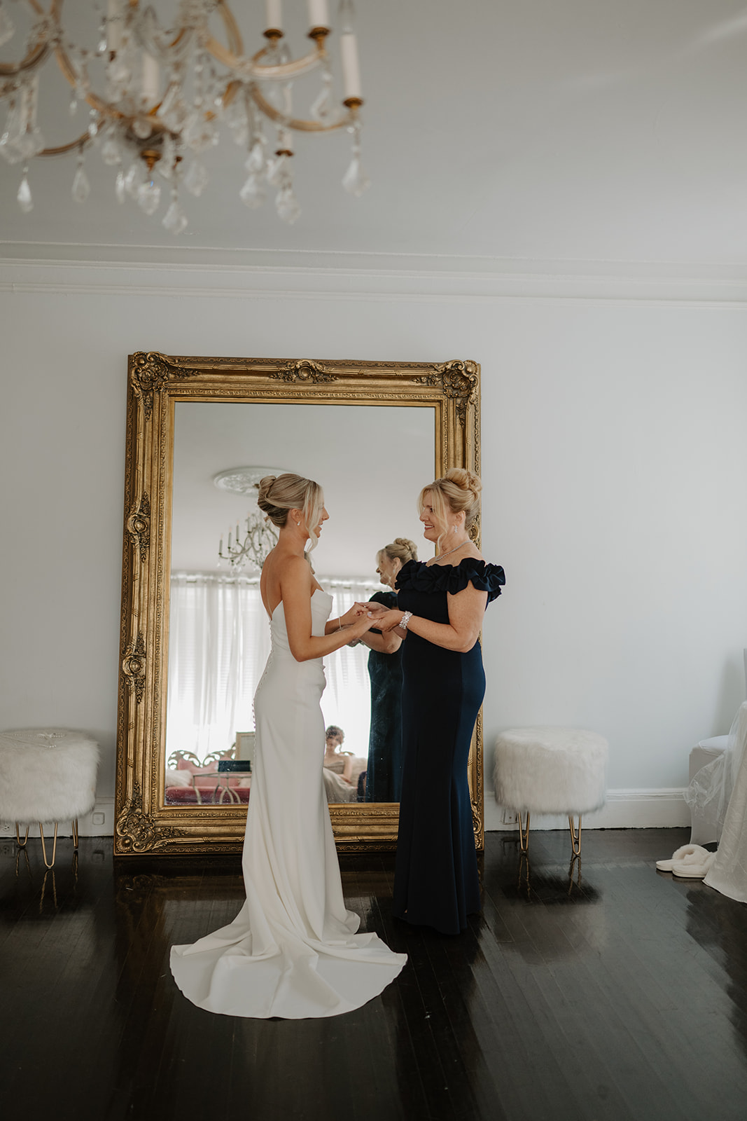 Bride and her mother hold hands and smile at each other, sharing a warm moment before the ceremony.